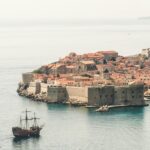 Brown Sailing Ship Near Building, Sure! Here’s a list of 6 items for your blog titled Where Travel Meets Adventure: Experiencing The Best of Dubrovnik, Croatia: **Explore the Ancient City Walls** Walk along Dubrovnik’s iconic city walls for breathtaking views of the Adriatic Sea and the stunning red-roofed buildings below. This historic fortification offers a unique perspective on the city's rich history and architecture. **Kayaking in the Adriatic Sea** Rent a kayak and paddle around the nearby islands and secluded beaches. This adventure allows you to experience the crystal-clear waters up close while enjoying the beauty of Dubrovnik's coastline from a different angle. **Take a Cable Car Ride to Mount Srđ** For panoramic views that will take your breath away, hop on the cable car to Mount Srđ. Once at the top, you can enjoy hiking trails, historical sites, and even dine at a restaurant with stunning vistas. **Visit Lokrum Island** A short boat ride from Dubrovnik, Lokrum Island is perfect for day trips filled with nature walks, swimming spots, and exploring historic ruins like an ancient Benedictine monastery. Don’t forget to visit the famous Dead Sea! **Discover Game of Thrones Filming Locations** For fans of the series, embark on a guided tour showcasing filming locations used in Game of Thrones. Visit iconic spots like Fort Lovrijenac (the Red Keep) and stroll through Old Town's streets where key scenes were shot. **Adventure through Cavtat’s Hiking Trails** Just south of Dubrovnik lies Cavtat, where scenic hiking trails wind through lush landscapes and offer spectacular sea views. Discover hidden coves and charming villages along your journey while soaking in Croatia’s natural beauty. These activities capture both travel experiences and adventurous undertakings that make Dubrovnik an unforgettable destination! Croatia