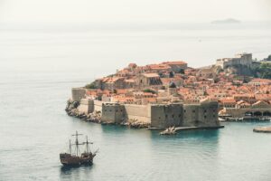 Brown Sailing Ship Near Building, Sure! Here’s a list of 6 items for your blog titled Where Travel Meets Adventure: Experiencing The Best of Dubrovnik, Croatia: **Explore the Ancient City Walls** Walk along Dubrovnik’s iconic city walls for breathtaking views of the Adriatic Sea and the stunning red-roofed buildings below. This historic fortification offers a unique perspective on the city's rich history and architecture. **Kayaking in the Adriatic Sea** Rent a kayak and paddle around the nearby islands and secluded beaches. This adventure allows you to experience the crystal-clear waters up close while enjoying the beauty of Dubrovnik's coastline from a different angle. **Take a Cable Car Ride to Mount Srđ** For panoramic views that will take your breath away, hop on the cable car to Mount Srđ. Once at the top, you can enjoy hiking trails, historical sites, and even dine at a restaurant with stunning vistas. **Visit Lokrum Island** A short boat ride from Dubrovnik, Lokrum Island is perfect for day trips filled with nature walks, swimming spots, and exploring historic ruins like an ancient Benedictine monastery. Don’t forget to visit the famous Dead Sea! **Discover Game of Thrones Filming Locations** For fans of the series, embark on a guided tour showcasing filming locations used in Game of Thrones. Visit iconic spots like Fort Lovrijenac (the Red Keep) and stroll through Old Town's streets where key scenes were shot. **Adventure through Cavtat’s Hiking Trails** Just south of Dubrovnik lies Cavtat, where scenic hiking trails wind through lush landscapes and offer spectacular sea views. Discover hidden coves and charming villages along your journey while soaking in Croatia’s natural beauty. These activities capture both travel experiences and adventurous undertakings that make Dubrovnik an unforgettable destination! Croatia